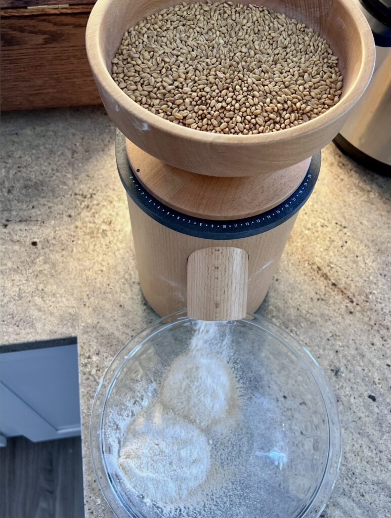 Freshly milled flour being prepared in a home kitchen using whole wheat berries, part of a simple from-scratch homemaking routine.