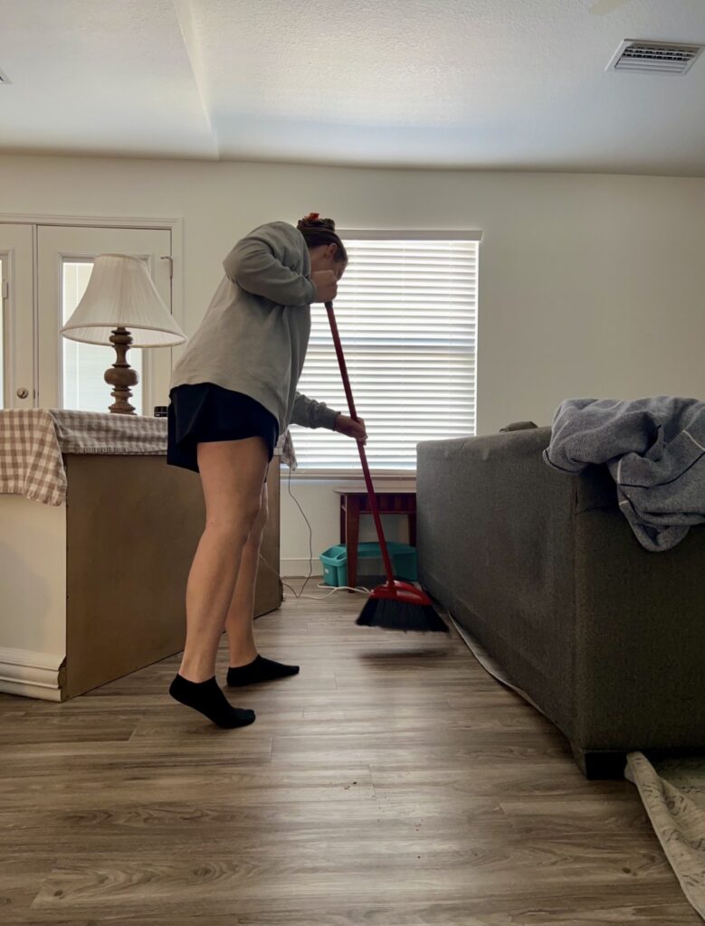 sweeping under couch during realistic spring cleaning routine for overwhelmed moms