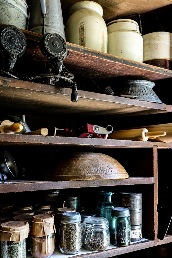 A rustic kitchen pantry scene with vintage jars, spices, and old cooking tools neatly organized on wooden shelves.